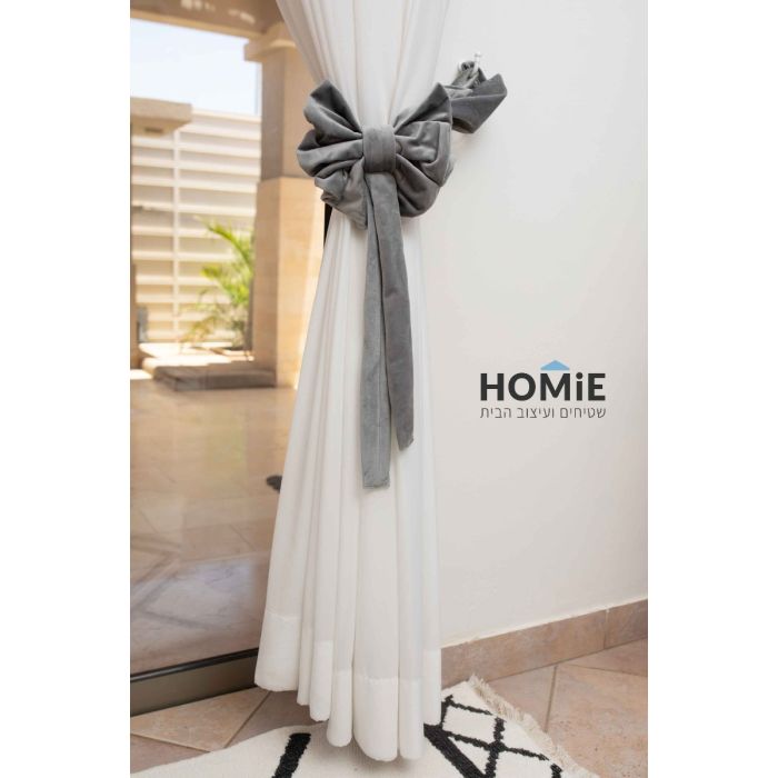 חבק פפיון דקורטיבי קטיפה לוילון בצבע אפור. החבק המהודר והיוקרתי המגיע בסגנון הרטרו כפרי ישדרג את מראה הוילון שלכם בכמה רמות ויאסוף אותו בצורה אפקטיבית ונעימה לעין. הוא מיוצר בעבודת יד על ידי אמן מוכשר שהשקיע בו עבודה מרובה. החבק יתאים לסלון, חדר שינה, חדר